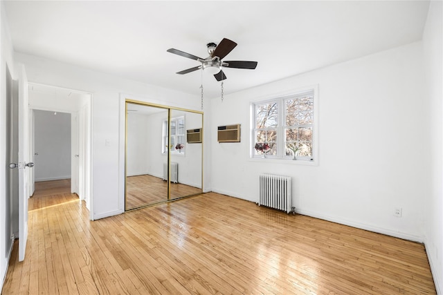 unfurnished bedroom featuring radiator, a wall unit AC, light hardwood / wood-style floors, and a closet