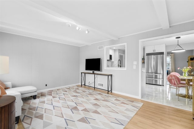 living area with visible vents, light wood-style flooring, beam ceiling, and baseboards