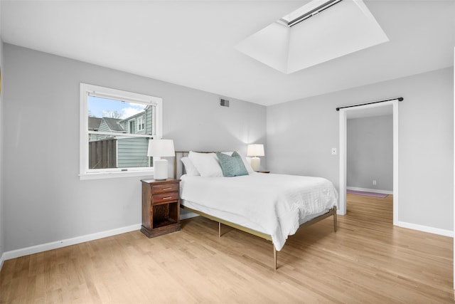 bedroom featuring light wood finished floors, a skylight, visible vents, and baseboards