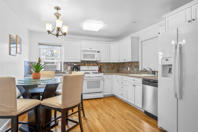 kitchen featuring white appliances, white cabinetry, backsplash, and a sink