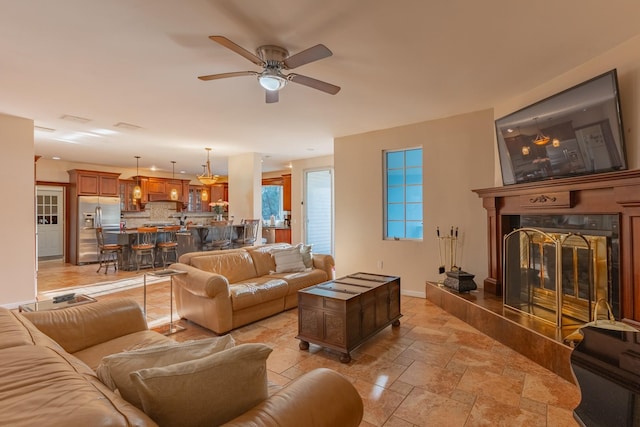 living area with stone tile flooring, a fireplace, ceiling fan, and baseboards