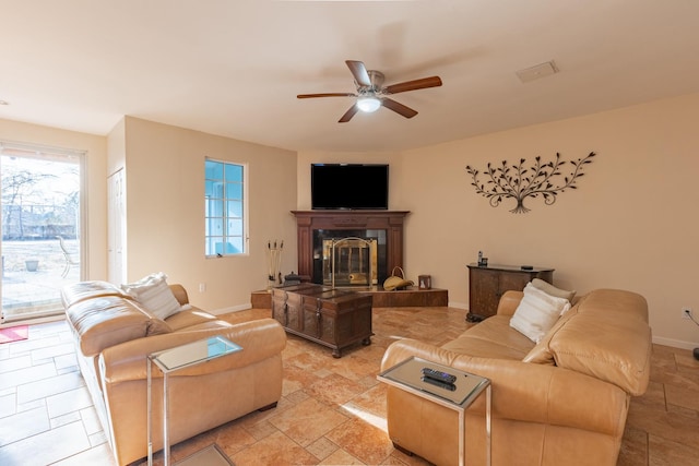 living room with a ceiling fan, stone tile flooring, a fireplace, and baseboards