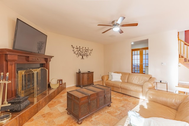 living room with baseboards, a fireplace with raised hearth, ceiling fan, stone finish floor, and stairs