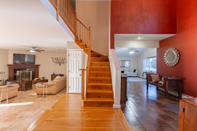 staircase featuring ceiling fan, a high ceiling, and a glass covered fireplace