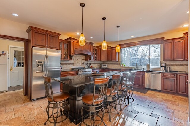 kitchen with stone tile flooring, a sink, appliances with stainless steel finishes, backsplash, and glass insert cabinets