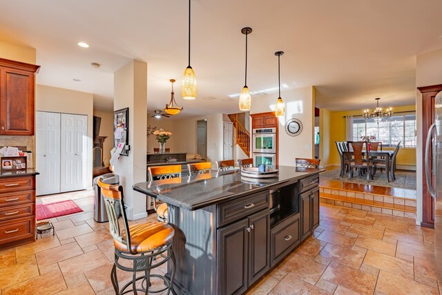 kitchen featuring dark countertops, a kitchen breakfast bar, hanging light fixtures, stone tile flooring, and double oven