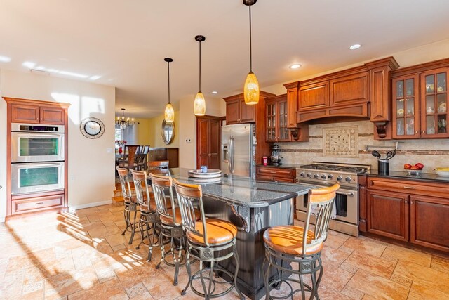 kitchen with stone tile flooring, backsplash, appliances with stainless steel finishes, brown cabinetry, and premium range hood