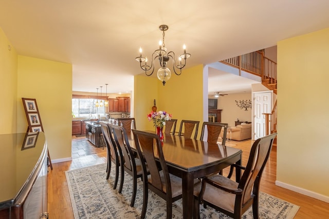 dining area featuring light wood-style floors, ceiling fan with notable chandelier, baseboards, and stairs