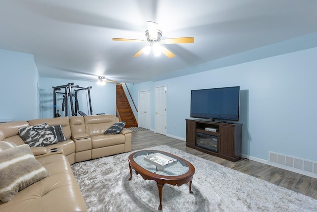 living area featuring baseboards, visible vents, a ceiling fan, wood finished floors, and stairs