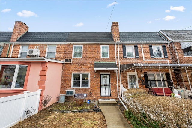 multi unit property featuring a chimney, roof with shingles, fence, ac unit, and brick siding