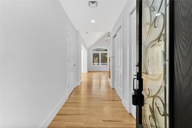 hall featuring lofted ceiling, an inviting chandelier, and light hardwood / wood-style flooring