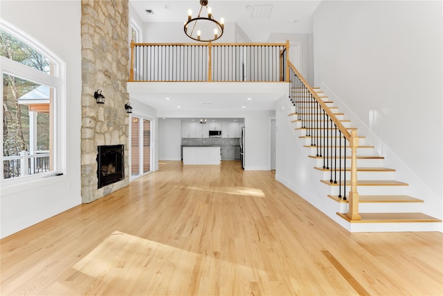 unfurnished living room with an inviting chandelier, a fireplace, a high ceiling, and light wood-type flooring