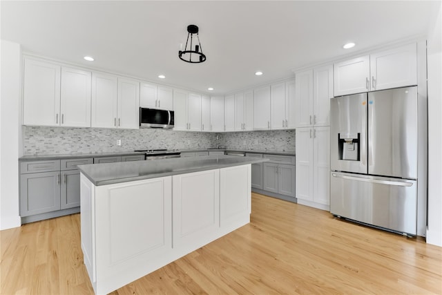 kitchen with white cabinetry, stainless steel appliances, decorative light fixtures, and light wood-type flooring