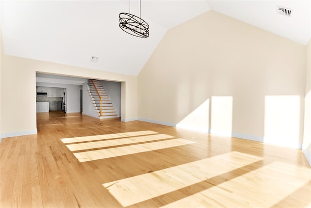 unfurnished living room featuring hardwood / wood-style floors, a notable chandelier, and high vaulted ceiling