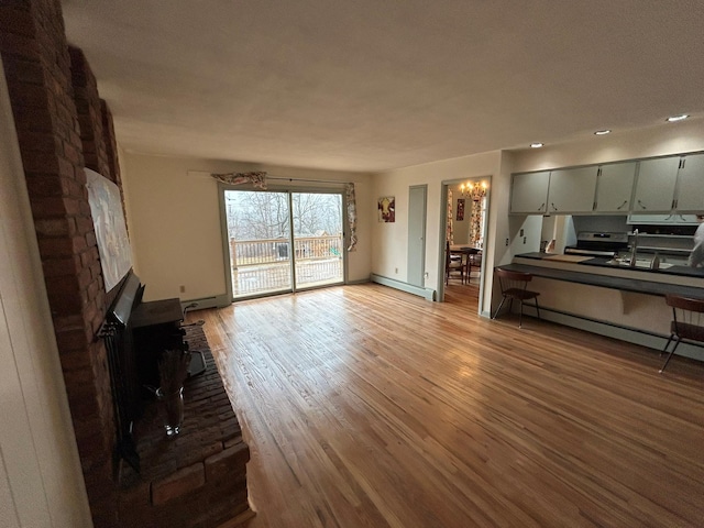 unfurnished living room with a baseboard heating unit, a notable chandelier, and hardwood / wood-style floors