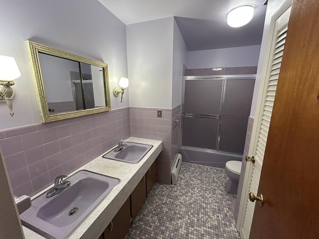 bathroom with toilet, combined bath / shower with glass door, tile walls, a baseboard radiator, and dual sinks