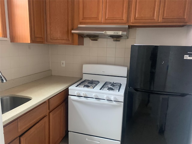 kitchen featuring sink, black refrigerator, tasteful backsplash, light stone countertops, and white gas stove