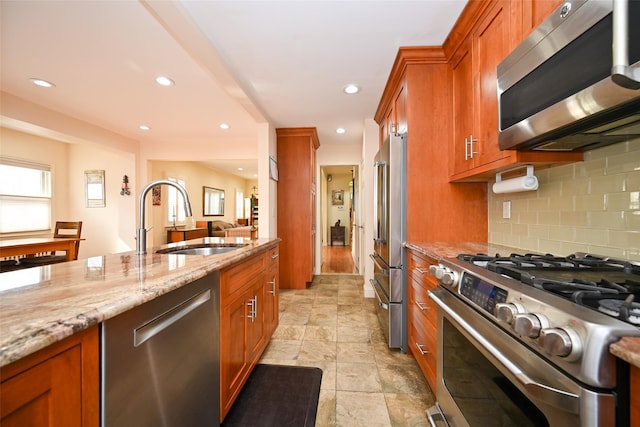 kitchen with appliances with stainless steel finishes, a sink, light stone counters, and brown cabinets