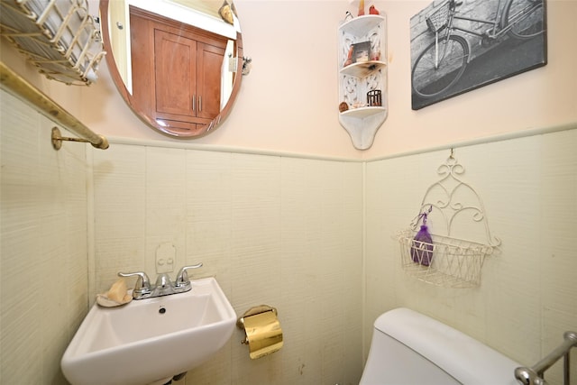 half bath with a sink, toilet, and tile walls