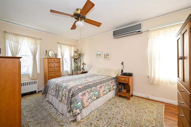 bedroom featuring baseboards, radiator, ceiling fan, wood finished floors, and a wall mounted air conditioner