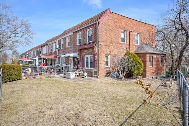 back of property featuring brick siding, a lawn, a patio area, and fence