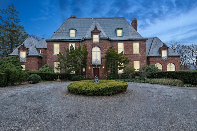 french country home with a high end roof, gravel driveway, and brick siding