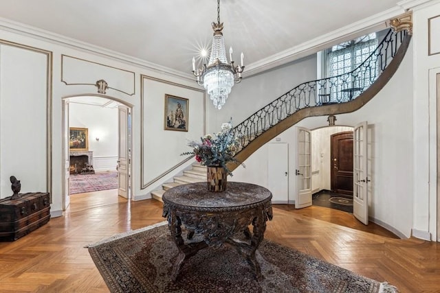 foyer entrance featuring a warm lit fireplace, arched walkways, stairway, an inviting chandelier, and crown molding