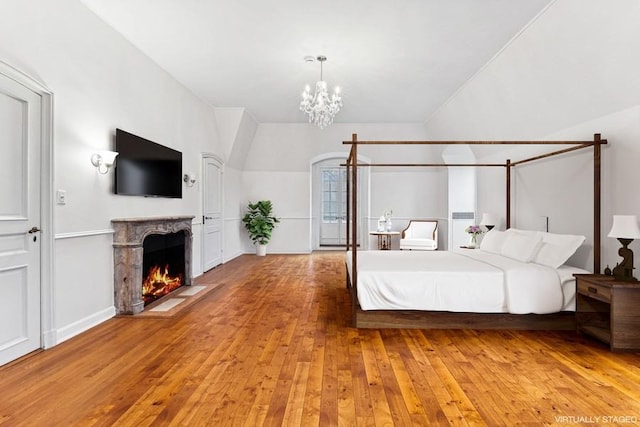 bedroom featuring a chandelier, hardwood / wood-style floors, a high end fireplace, and baseboards