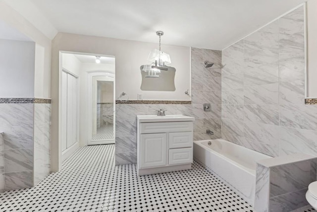 full bath with a notable chandelier, vanity, tile walls, wainscoting, and tub / shower combination