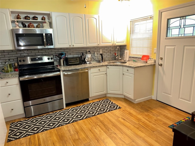 kitchen featuring sink, white cabinetry, light wood-type flooring, appliances with stainless steel finishes, and backsplash