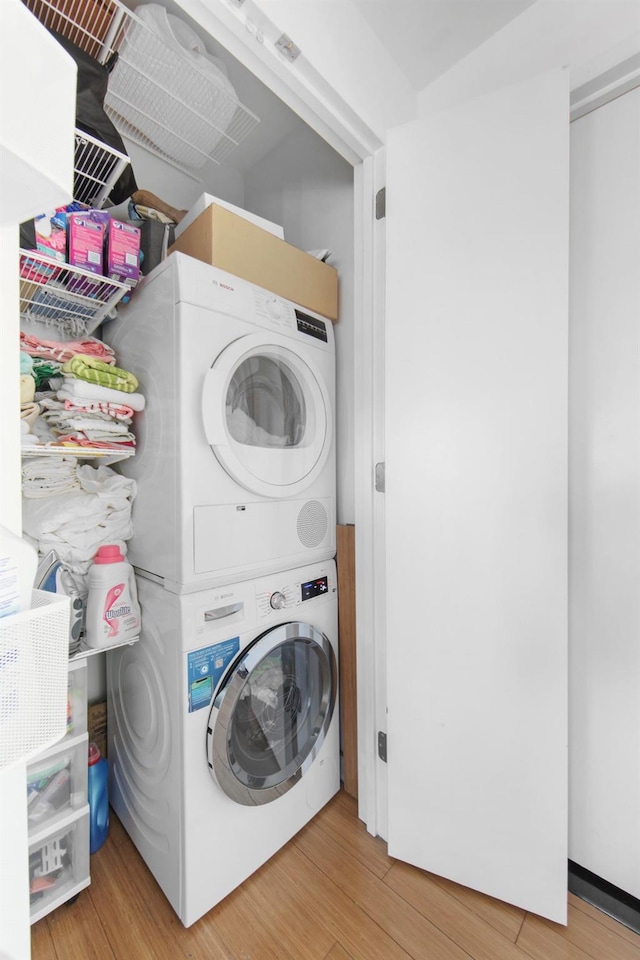 washroom with stacked washer and dryer and light hardwood / wood-style flooring