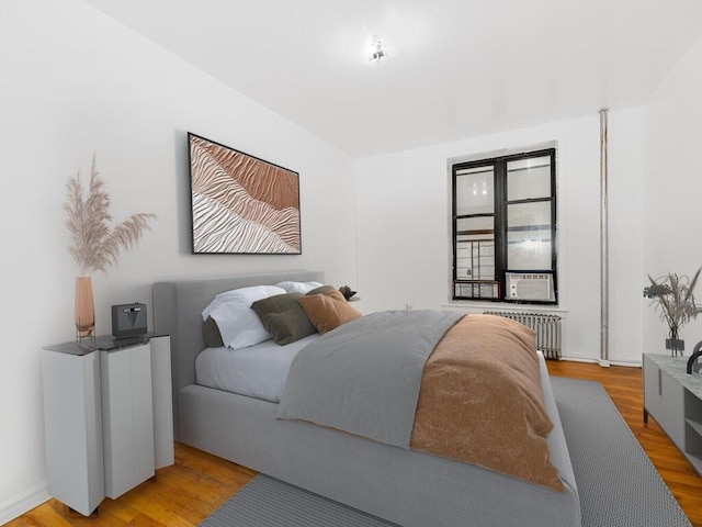 bedroom featuring cooling unit, radiator heating unit, and light wood-type flooring