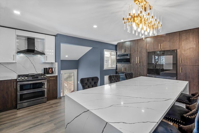 kitchen featuring pendant lighting, wall chimney range hood, double oven range, white cabinets, and a kitchen bar