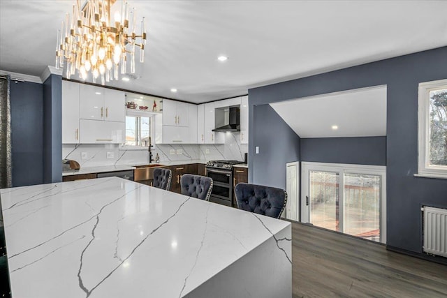 kitchen with white cabinetry, hanging light fixtures, appliances with stainless steel finishes, light stone countertops, and wall chimney range hood