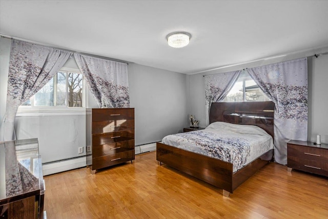 bedroom with multiple windows, a baseboard heating unit, and light wood-type flooring