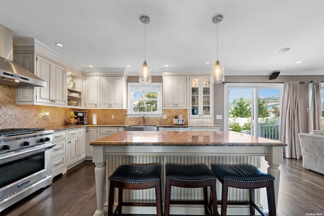 kitchen featuring wall chimney exhaust hood, high end stainless steel range, sink, decorative light fixtures, and a center island