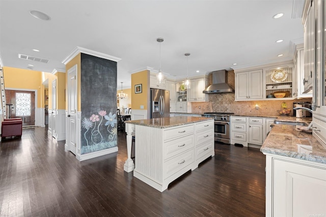 kitchen with hanging light fixtures, a kitchen island, stainless steel appliances, light stone countertops, and wall chimney range hood