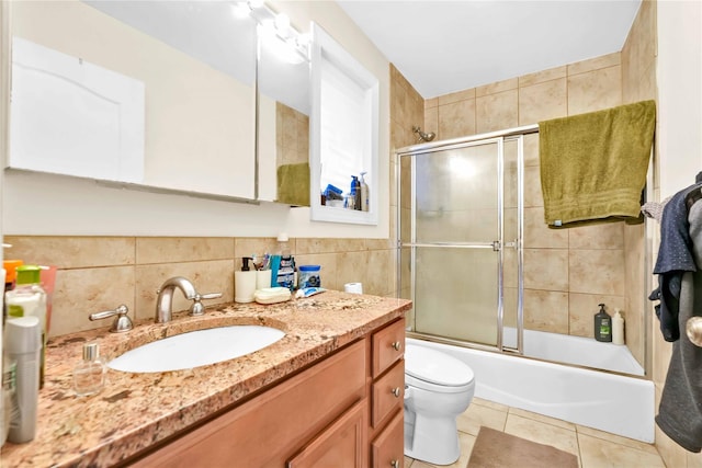 full bathroom with tile walls, tile patterned flooring, bath / shower combo with glass door, vanity, and toilet