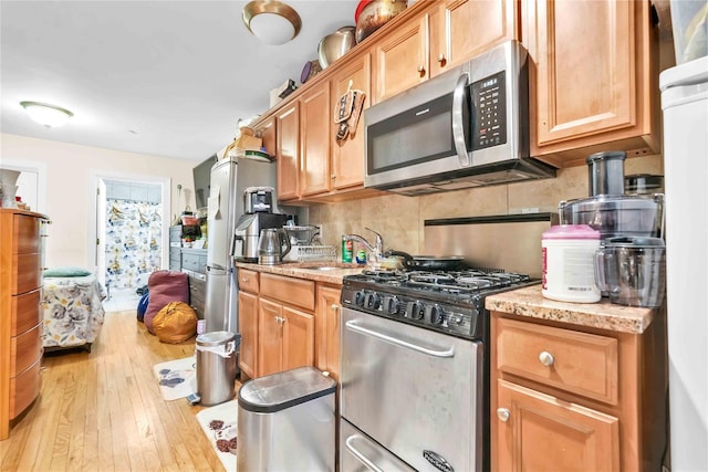 kitchen with sink, light hardwood / wood-style flooring, stainless steel appliances, light stone countertops, and decorative backsplash