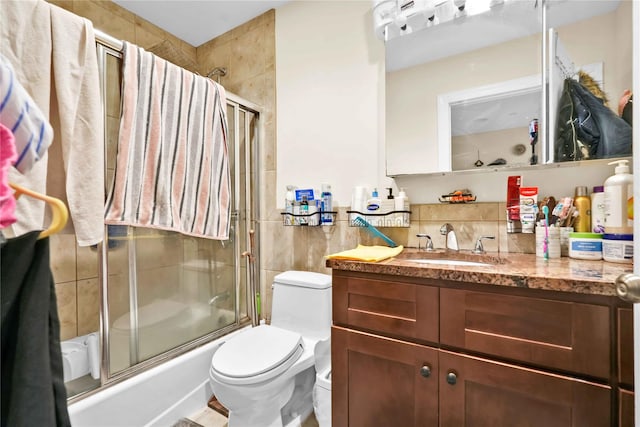 full bathroom with vanity, tile walls, shower / bath combination with glass door, and toilet