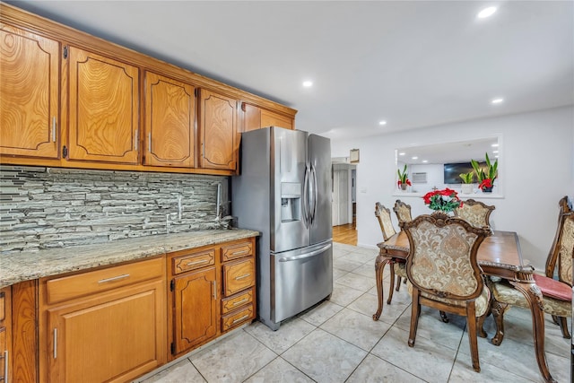 kitchen with light stone counters, backsplash, light tile patterned floors, and stainless steel refrigerator with ice dispenser