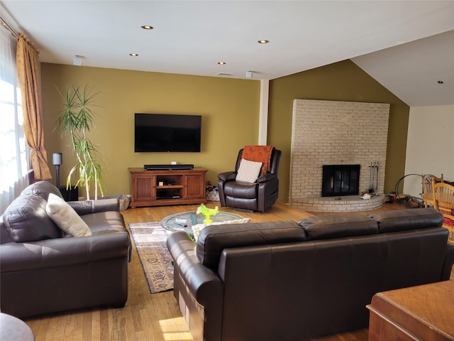 living room featuring vaulted ceiling, a brick fireplace, and light wood-type flooring