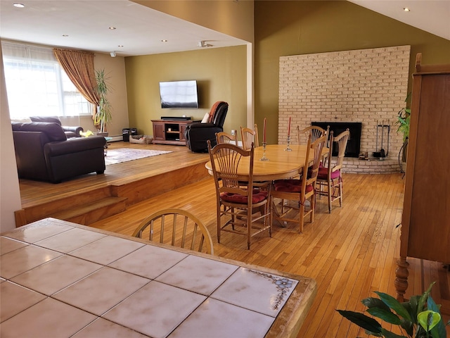 dining room featuring a brick fireplace, lofted ceiling, and light hardwood / wood-style floors