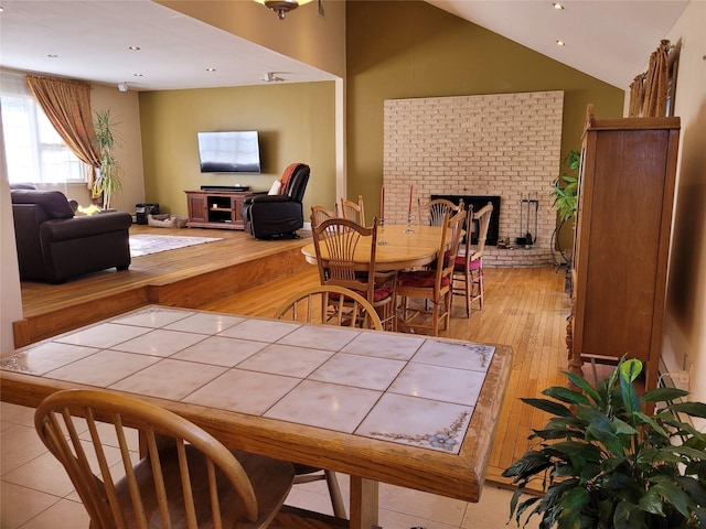 dining room featuring lofted ceiling, a brick fireplace, and light hardwood / wood-style floors