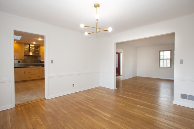 spare room with wood-type flooring, ornamental molding, and a chandelier