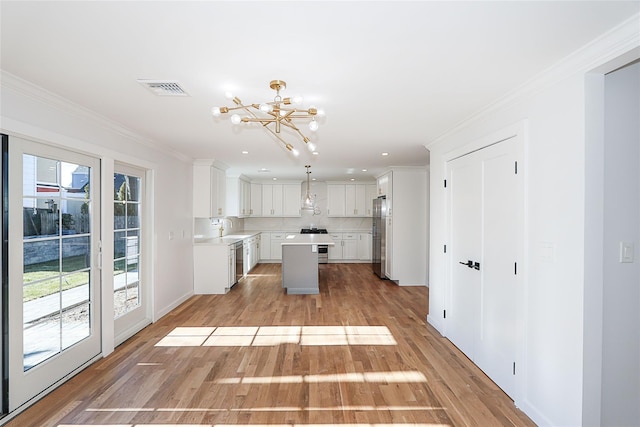 kitchen with appliances with stainless steel finishes, white cabinetry, hanging light fixtures, ornamental molding, and a kitchen island