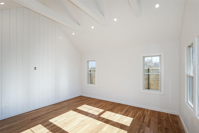 empty room featuring lofted ceiling with beams, a healthy amount of sunlight, and dark wood-type flooring