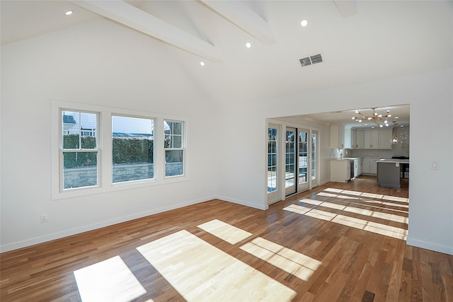 unfurnished living room featuring hardwood / wood-style flooring, an inviting chandelier, beam ceiling, and high vaulted ceiling