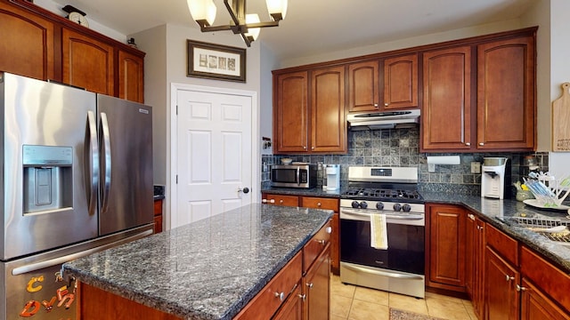 kitchen featuring a center island, under cabinet range hood, dark stone counters, decorative backsplash, and stainless steel appliances