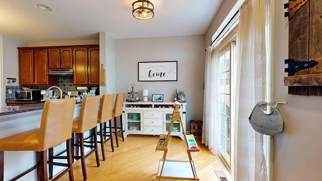 kitchen with stainless steel microwave, tasteful backsplash, light wood-type flooring, visible vents, and a breakfast bar area